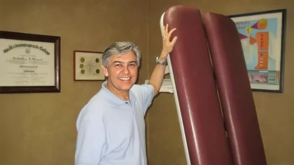 Chiropractor Burbank CA Jorge Silverio Poses Next to an Adjustment Table That is Folded Up Jorge Silverio Poses Next to an Adjustment Table That is Folded Up